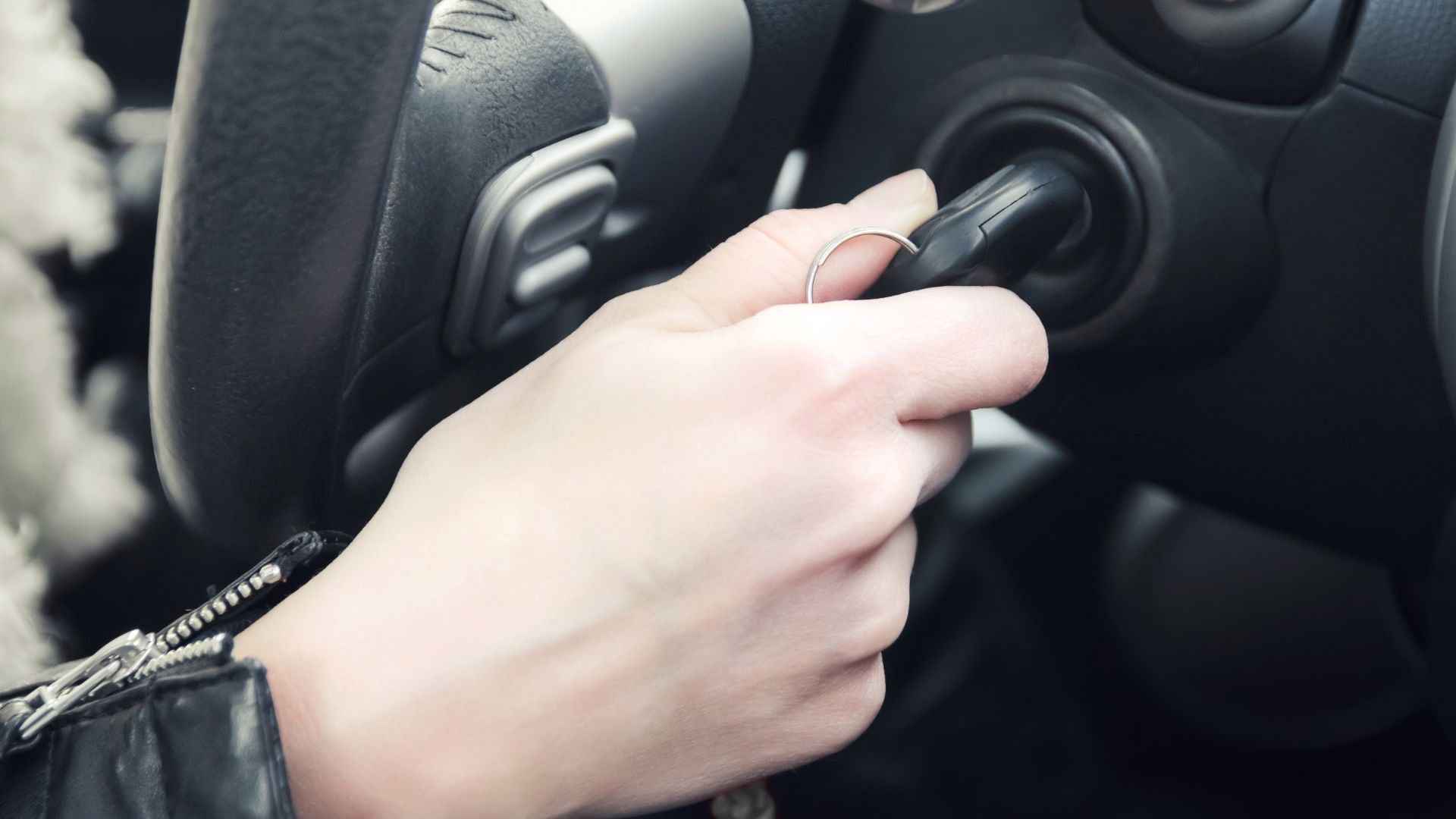 a person holding a cell phone while driving a car.|a close up of a car's steering wheel and dashboard.