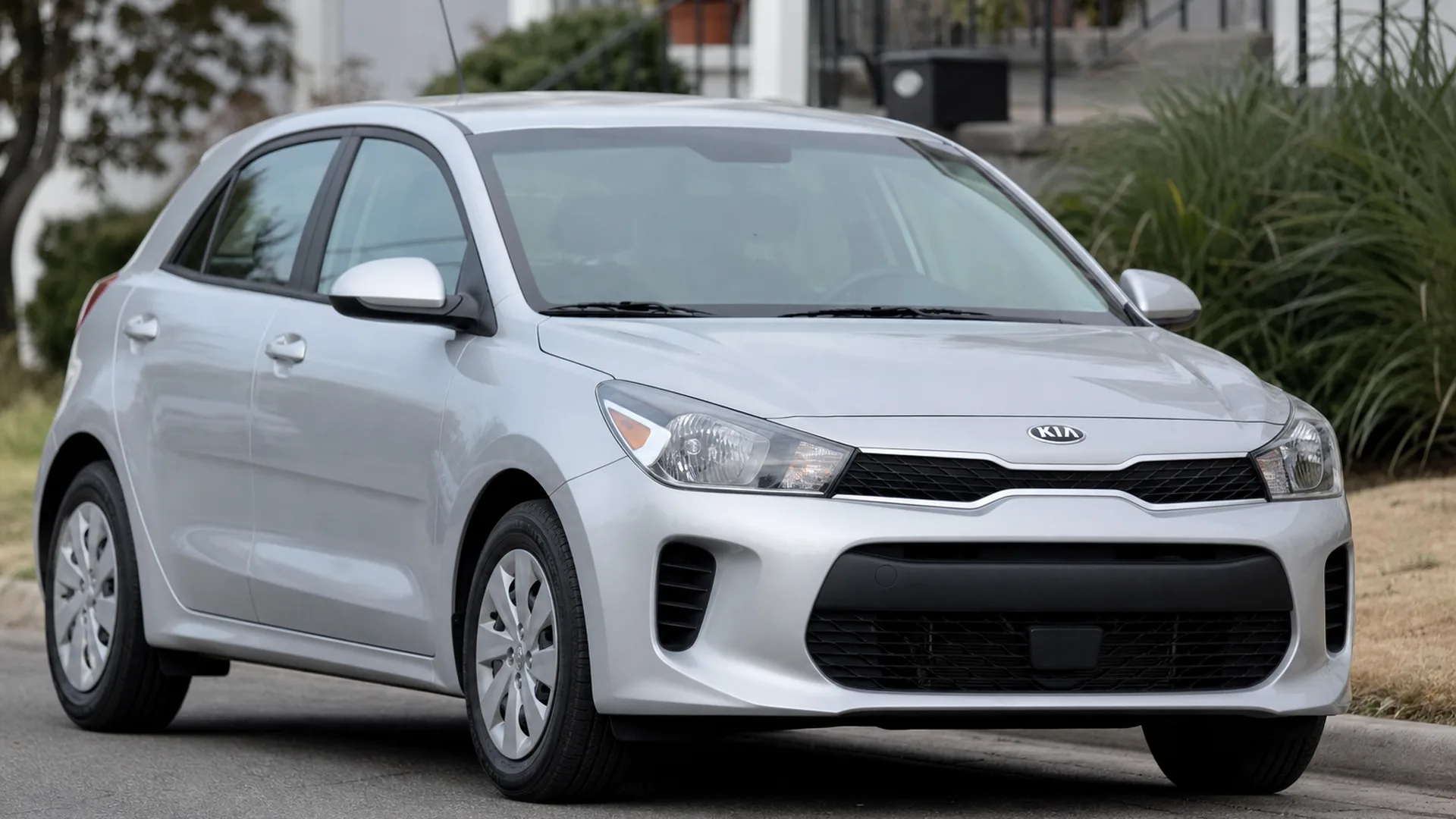 A silver Kia Rio hatchback parked on a residential street.