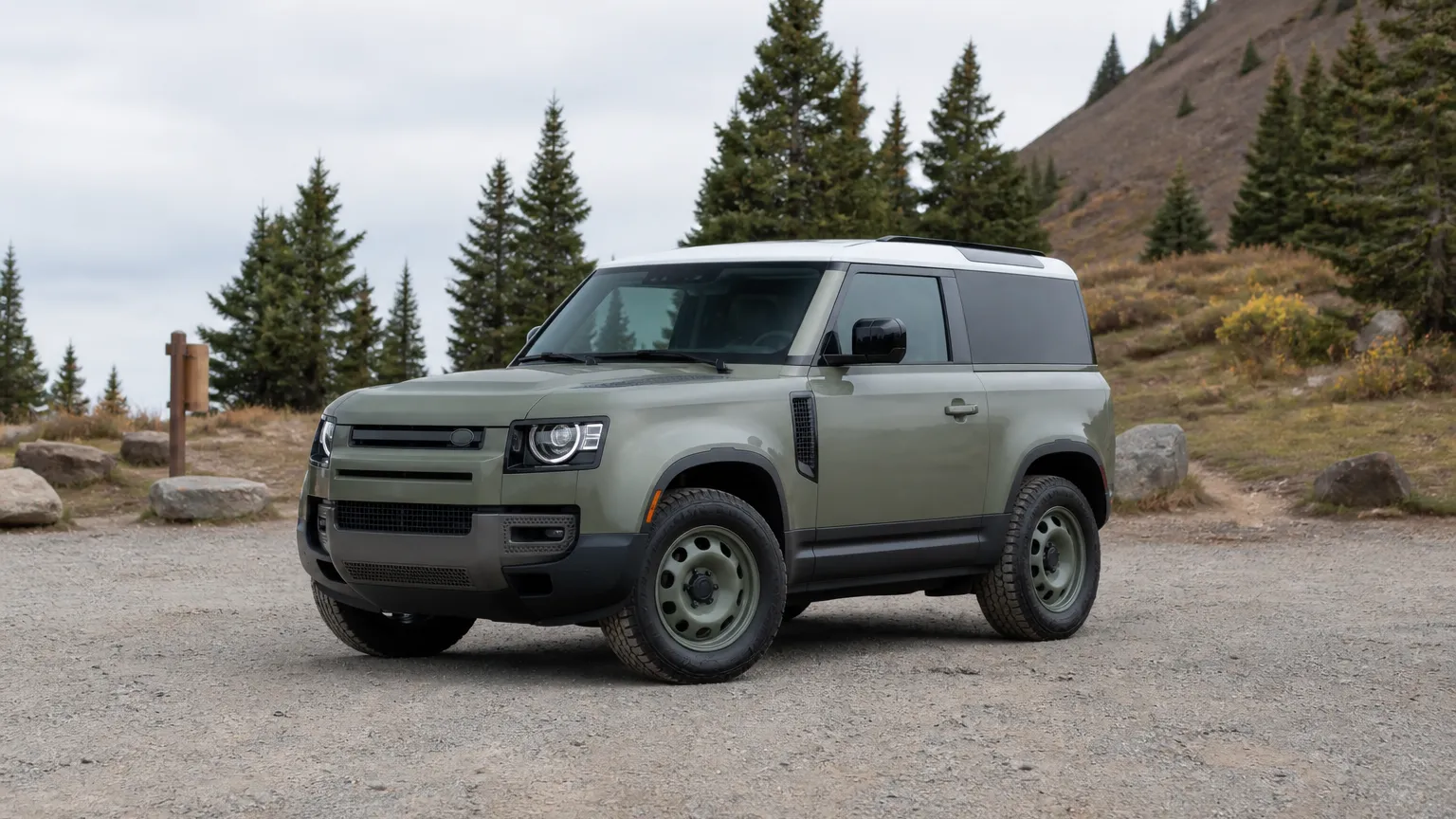 A Land Rover Defender off-road SUV, three-quarter front view, parked on a gravel trailhead.