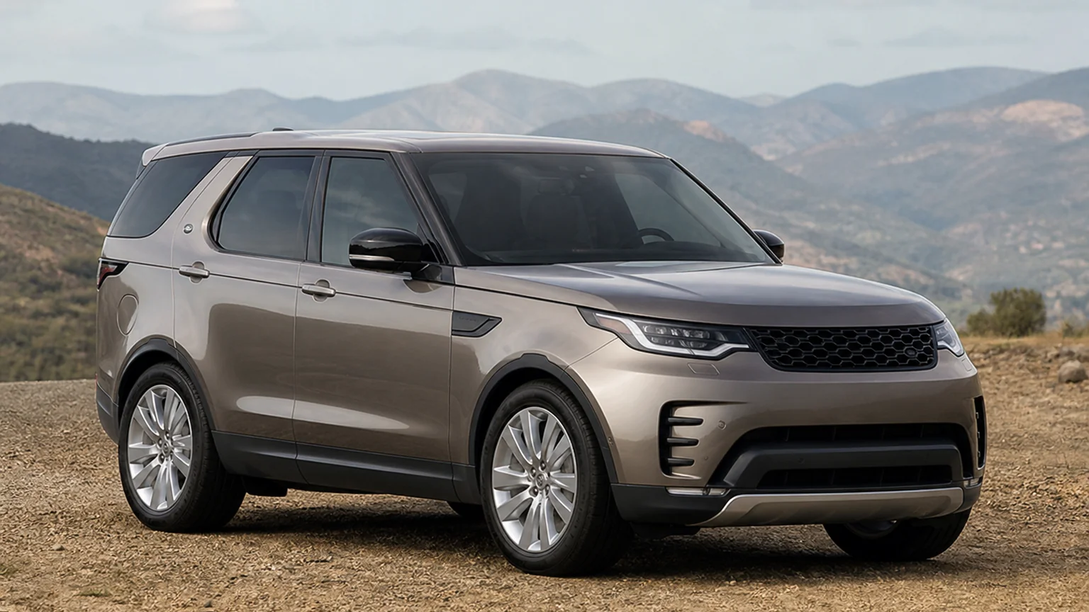 A Land Rover Discovery three-row SUV, three-quarter front view, parked on a quiet street.