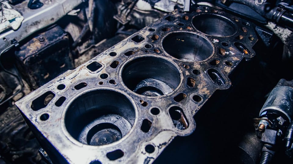 a close up of an old engine block.|a close up of an old engine block.|a man working on an engine in a garage.|a close up of an engine block on a car.|a close up of an engine block in a vehicle.