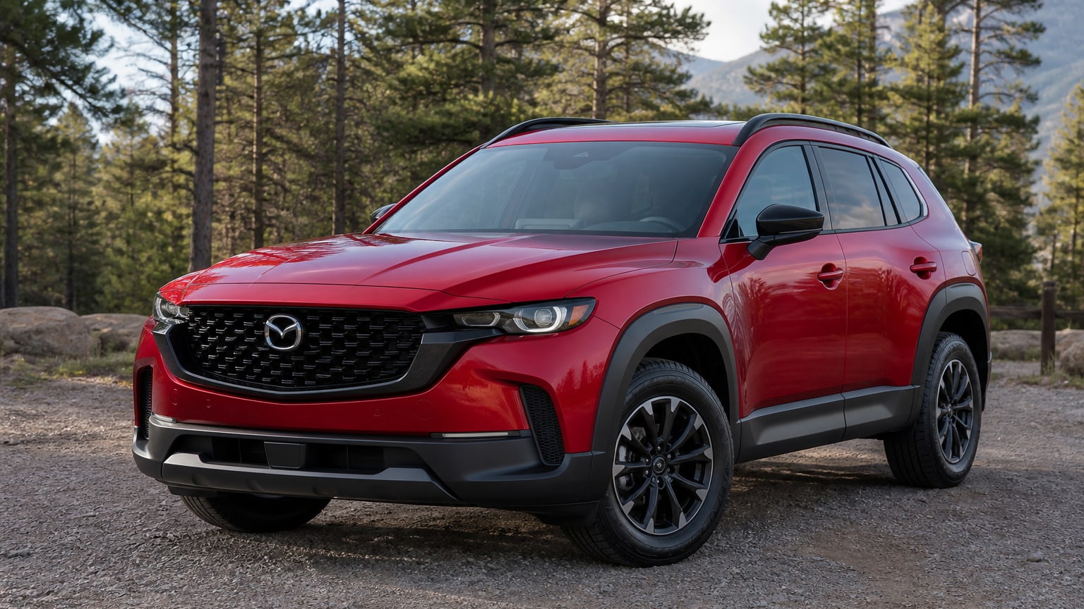 A red Mazda CX-50 crossover parked at a trailhead lot.