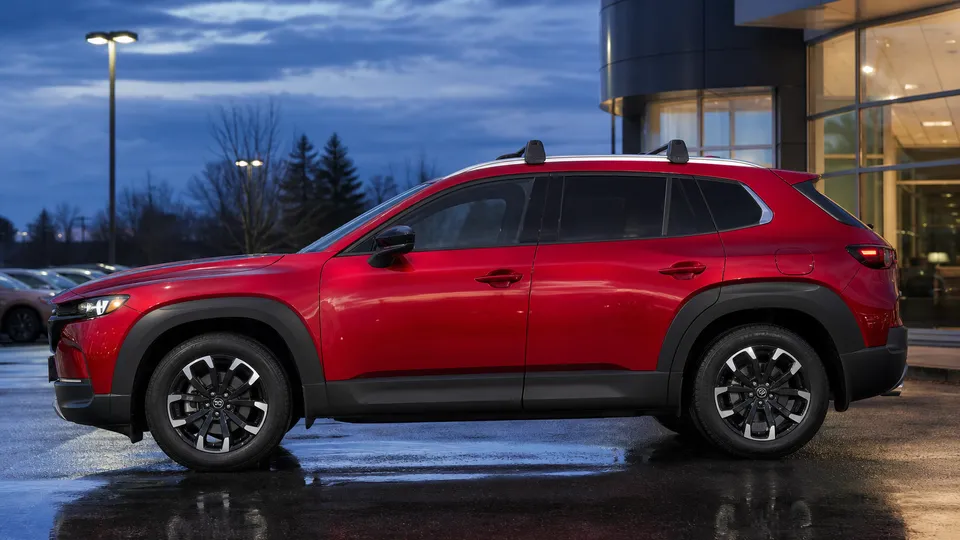 A red Mazda CX-50 crossover parked at a trailhead lot.