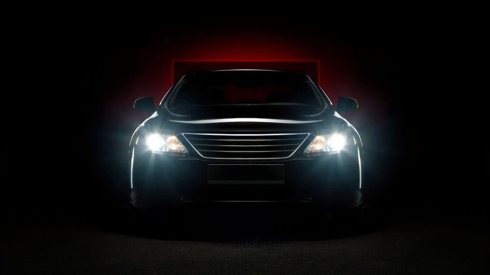 a car with its headlights on in the dark.|a person holding a small light bulb in their hand.|a close up of the headlight of a blue car.|a close up of the headlights of a blue car.|a close up of the front of a car.|the front lights of a car in the dark.