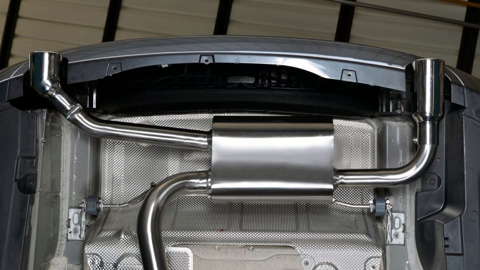 a close up of a metal object in a garage.|a close up of a exhaust pipe on a vehicle.|a close up of a metal pipe with a green wall in the background.