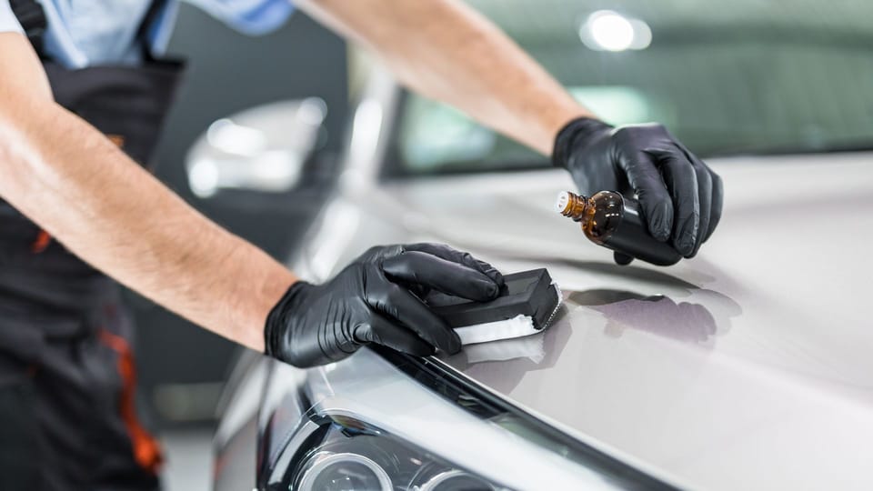 a man polishing the hood of a car.|a person waxes a car with a cloth.