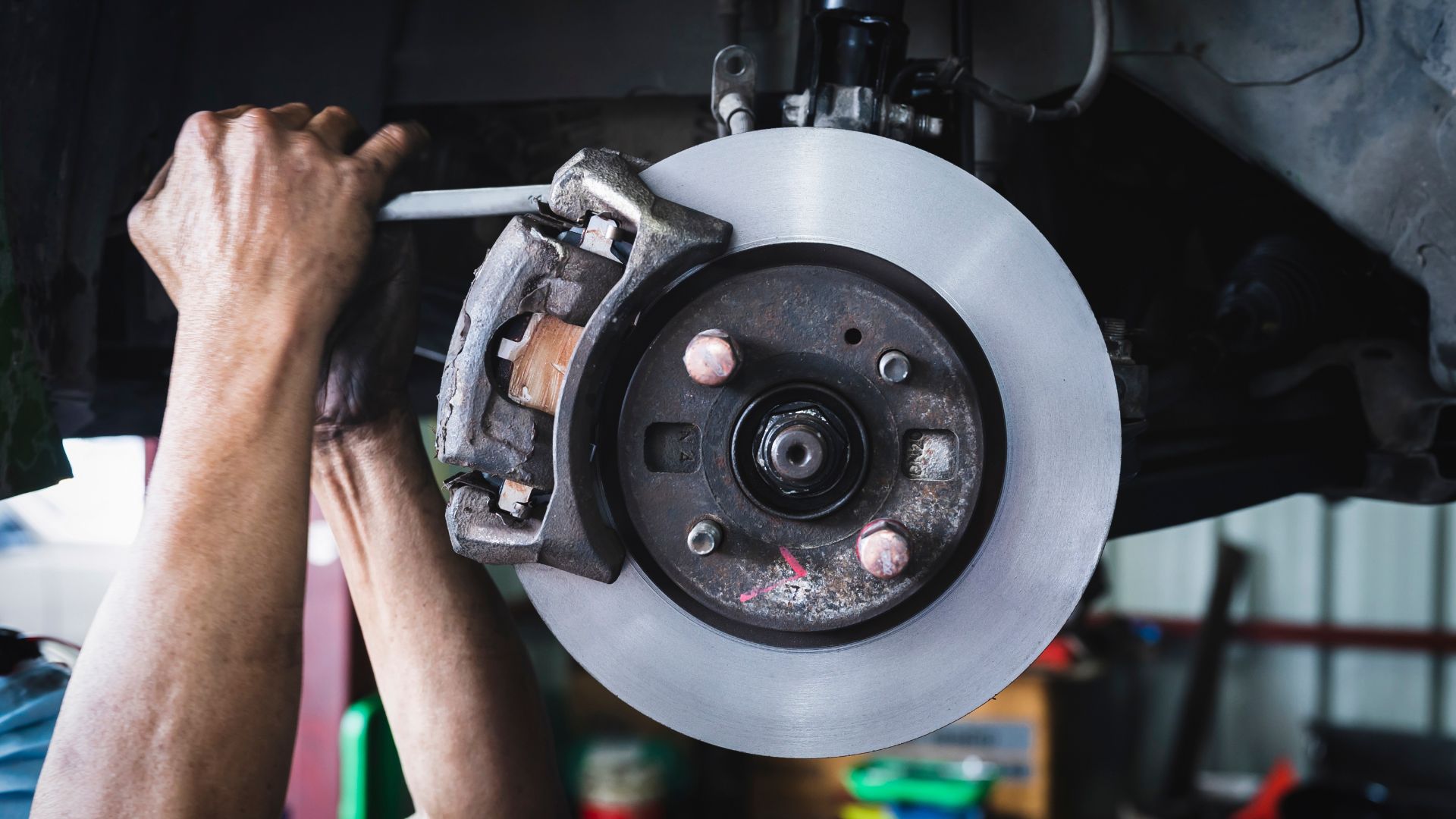 a man working on a brake assembly in a garage.|a close up of a brake on a vehicle.