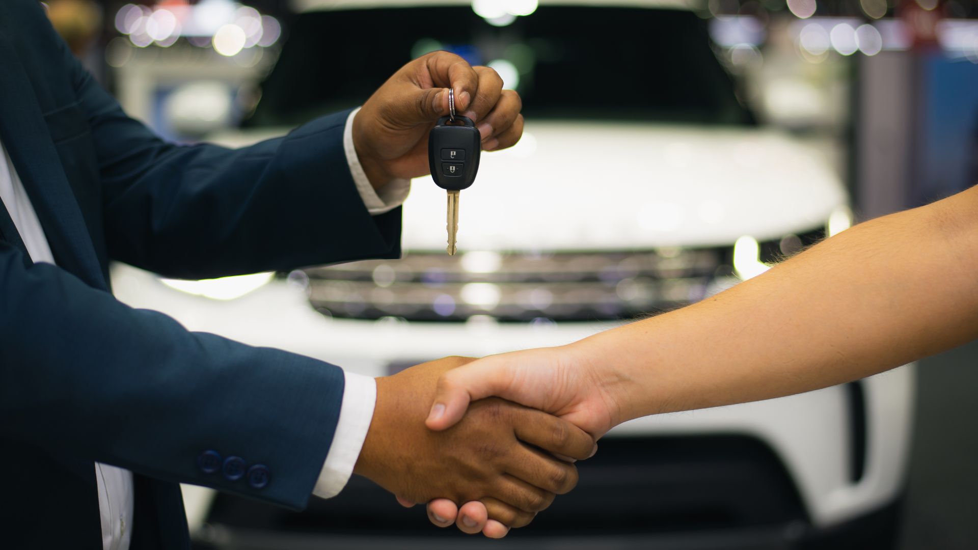 a couple of people shaking hands in front of a car.|a car key sitting on top of a pile of money.