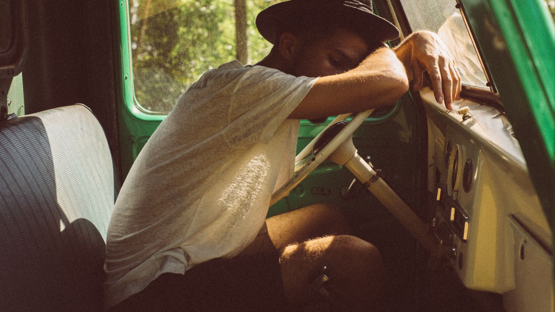 a person sitting in the back seat of a van.|a man sitting in the back of a green truck.|a couple of sleeping bags in the back of a truck.