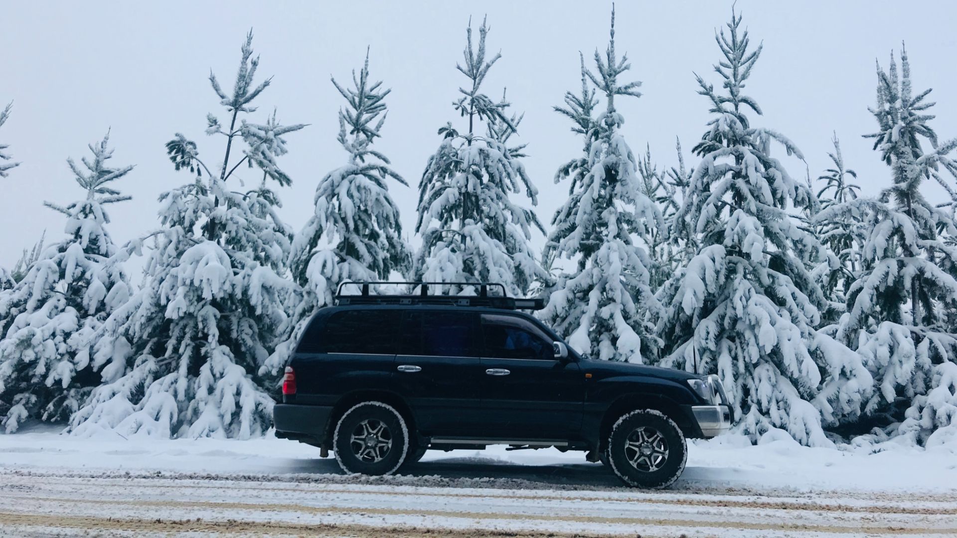 a black truck driving down a snow covered road.|a truck is driving through the mud in the desert.