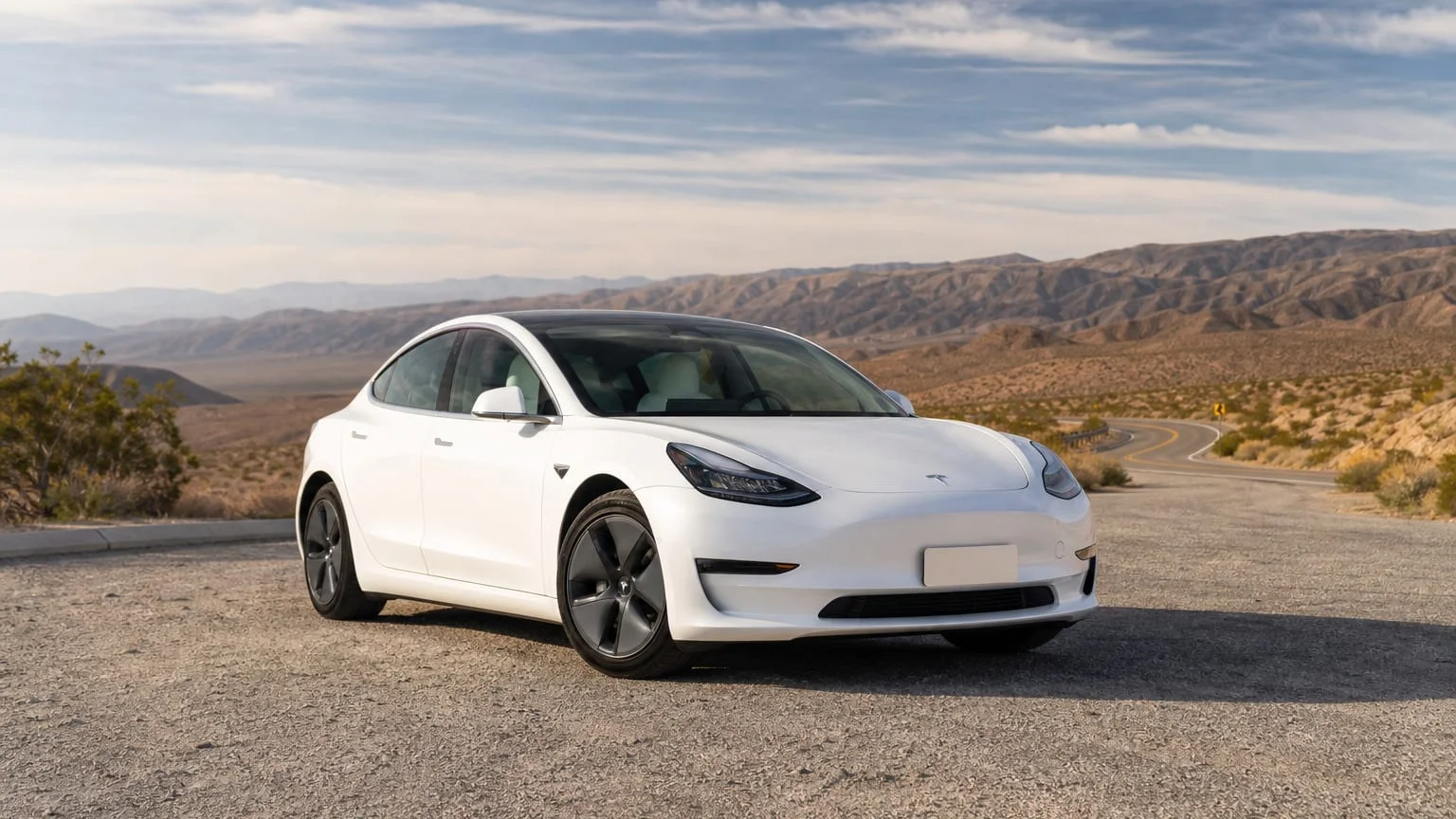 A Tesla Model 3 compact electric sedan, three-quarter front view, parked on a quiet street.