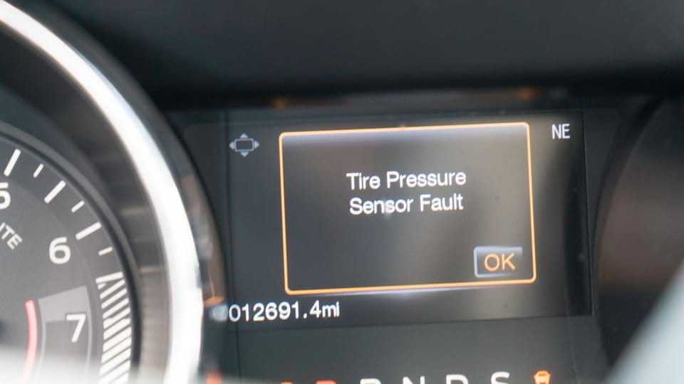 a close up of a gauge on a car.|a black and yellow logo with the words check tire pressure.|a close up of a person standing next to a car tire.