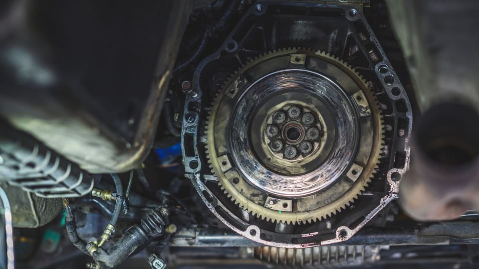 a close up of a metal gear on a vehicle.|a car being worked on in a garage.|a close up of a metal object with a wrench.|a close up of a car engine with wires.|the engine compartment of a vehicle with the top part of the engine exposed.