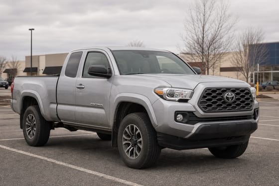Silver Toyota Tacoma pickup truck parked in a suburban shopping center lot on an overcast day.