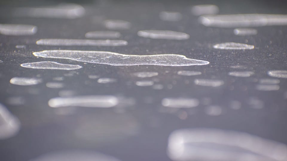 a close up of a table with a lot of bubbles on it.|a pair of scissors sitting on top of a car mirror.|a red car covered in snow with a brush.